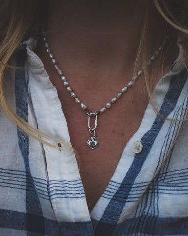 Close-up of a person wearing a pearl necklace with a beet root pendant, blurred background