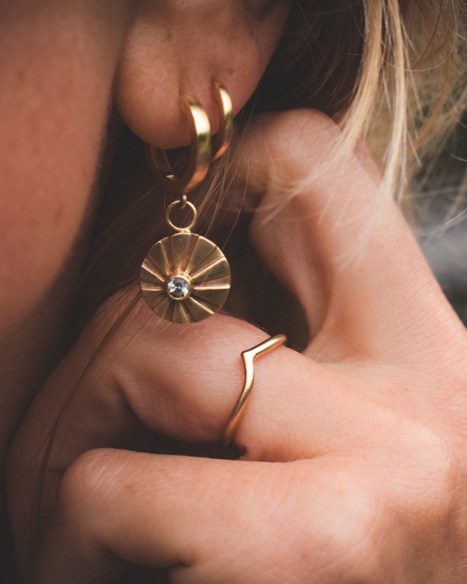 A person wearing a gold hoop earring with a central sapphire stone, surrounded by smaller sapphire stones on the hoop.