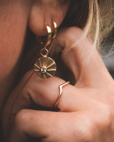 A person wearing a gold hoop earring with a central sapphire stone, surrounded by smaller sapphire stones on the hoop.