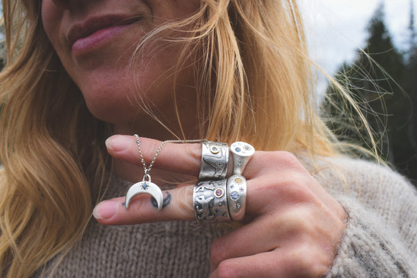 Close-up of a person wearing silver rings and a necklace with a crescent moon pendant.