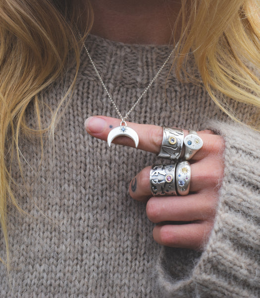 Person wearing a silver necklace and multiple rings on a neutral background