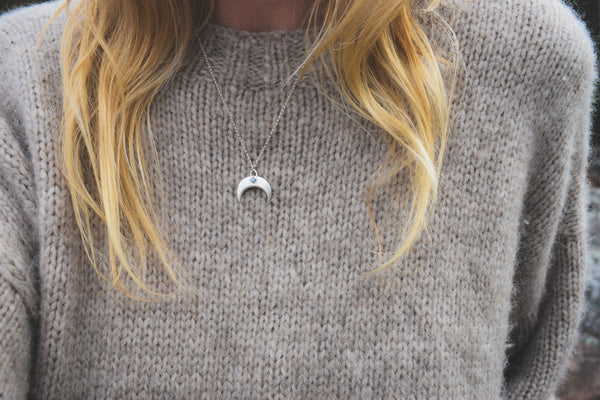 Person wearing a brown knitted sweater with a necklace featuring a crescent moon pendant.