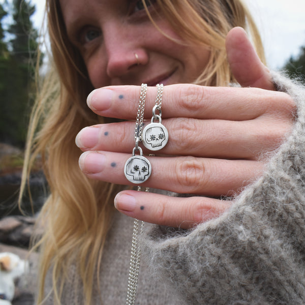 Person holding a silver necklace with two pendant charms outdoors