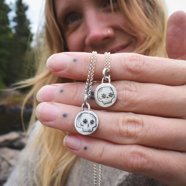 Person holding two silver necklaces with pendants outdoors