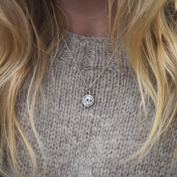 Necklace with a skull pendant worn by a person with blonde hair, against a neutral background.