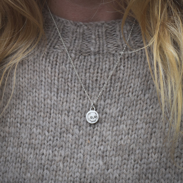 Close-up of a person wearing a silver necklace with a pendant on a gray knitted sweater.