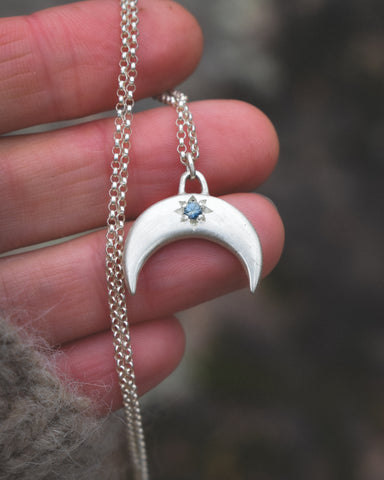 Silver necklace with a crescent moon pendant held in a hand against a blurred background