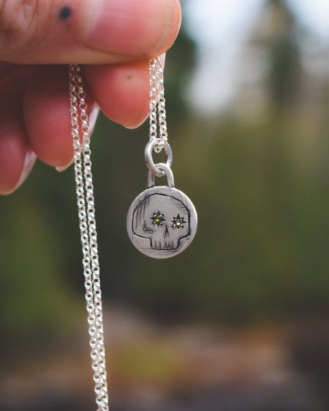 Silver necklace with a skull pendant held by a hand against a blurred natural background