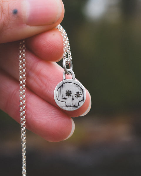 Silver necklace with a skull pendant held by a hand against a blurred background