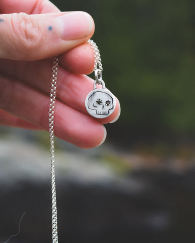 Silver necklace with a pendant held by a hand against a blurred natural background